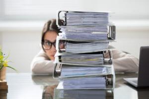 woman hiding behind a stack of folders on desk.